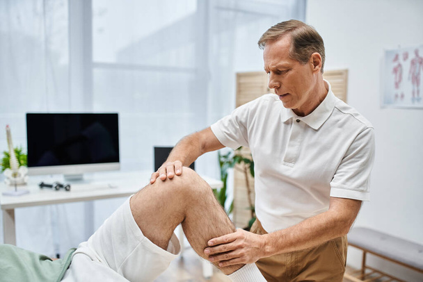gut aussehender, reifer Arzt untersucht Knie seines Patienten im Krankenhaus, Rehabilitationskonzept - Foto, Bild