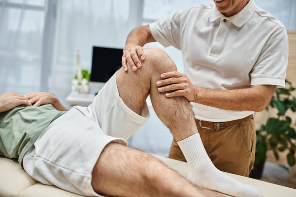 good looking mature doctor checking up knees of his patient in hospital, rehabilitation concept - Photo, Image