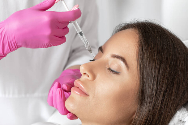 The doctor does injections to correct the hump on the nose with the beauty of the blonde. The beautician doees injections against wrinkles on the face. Women's cosmetology in a beauty salon. - Photo, Image