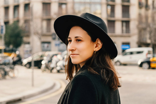 Chill νεαρή γυναίκα φορώντας μαύρο καπέλο είναι το περπάτημα μέσα από μια ευρωπαϊκή πόλη. Εξωτερικό πορτρέτο. - Φωτογραφία, εικόνα