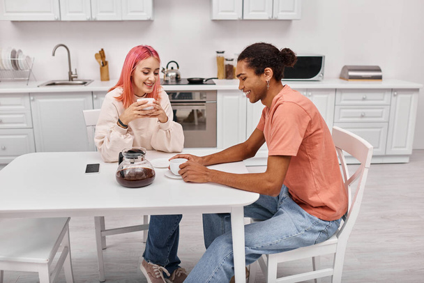 bom olhar alegre casal diverso sentado à mesa com café e olhando um para o outro - Foto, Imagem