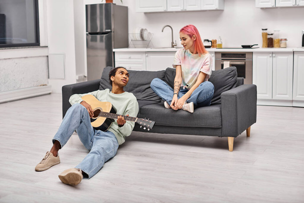 ハンサムなアフリカ系アメリカ人男性はギターを弾き,彼のピンクのハイレッドガールフレンドに愛情を持って見ています - 写真・画像