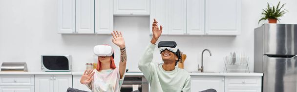 привлекательная веселая межрасовая пара, сидящая на диване в гостиной дома с VR гарнитурами, баннером - Фото, изображение