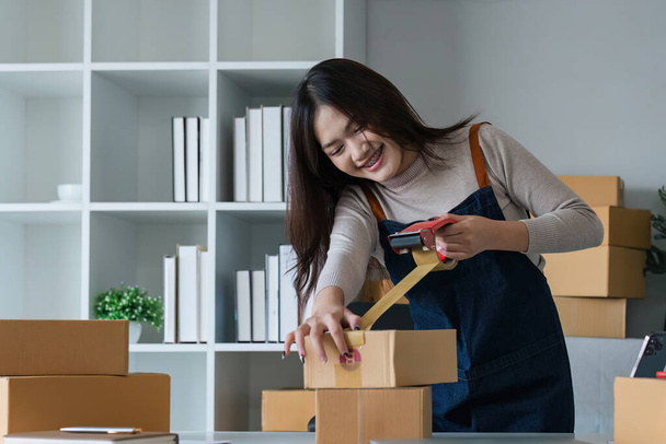 Mujer asiática joven tapando una caja de cartón en la oficina del hogar PYME e-commerce business, relocation and new small business concept, SME concept. - Foto, Imagen