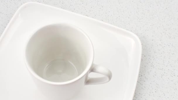 Bílý porcelánový pohár v detailu na lehkém povrchu, vyzařující rafinovanou jednoduchost okamžiku. - Záběry, video