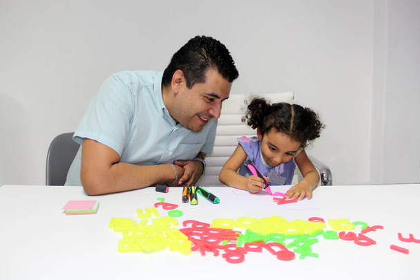 Rozvedený svobodný táta se svou brunetkou Latino kudrnaté vlasy dcera dělat domácí úkol, hrát, bavit se a strávit kvalitní čas - Fotografie, Obrázek