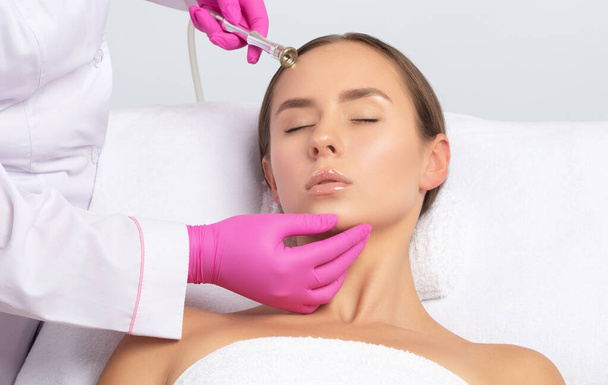 The cosmetologist makes the procedure Microdermabrasion of the face skin of a beautiful girl in a beauty salon.Cosmetology and professional skin care. - Photo, Image