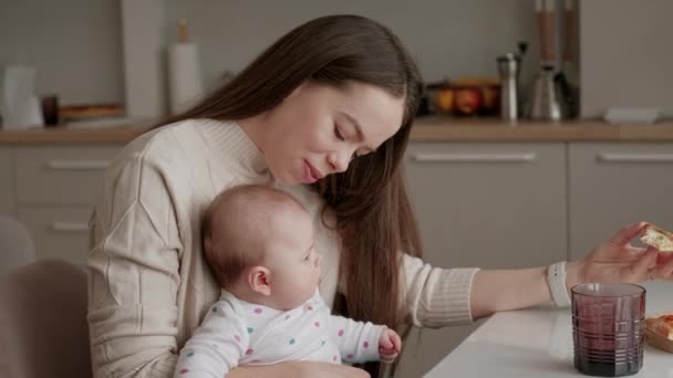 Felvételek fiatal anya ül a baba lány a konyhában, és eszik egy szelet pizza. - Felvétel, videó