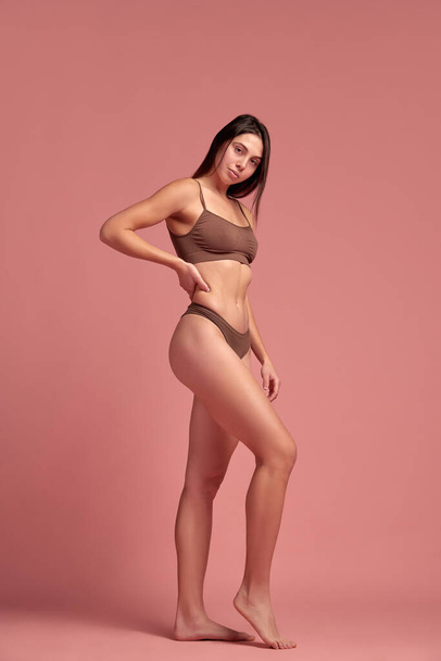 Loosing weight in healthy way. Young beautiful woman with slim body standing in cotton underwear against pink studio background. Concept of natural beauty, health and body care, diet, nutrition - Photo, Image