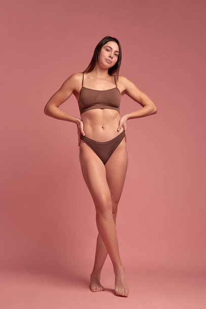 Health and nutrition. Full-length of attractive young woman with slim, healthy body standing in underwear against pink background. Concept of natural beauty, body care, diet, sport, wellness - Foto, Imagen