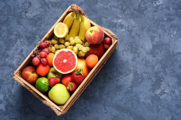 Деревянный ящик с различными свежими фруктами на синем фоне - Фото, изображение