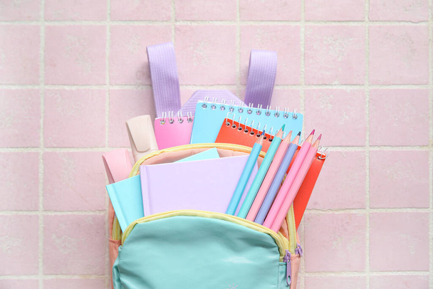 Цветной школьный рюкзак с блокнотами, карандашами и маркерами на розовом фоне плитки - Фото, изображение