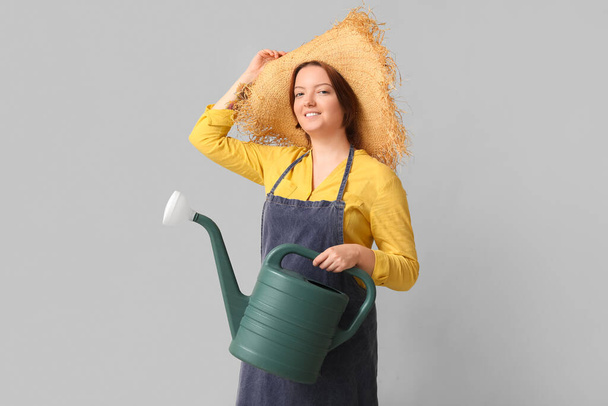 Χαμογελαστή γυναίκα σε ψάθινο καπέλο με ποτιστήρι σε γκρι φόντο - Φωτογραφία, εικόνα