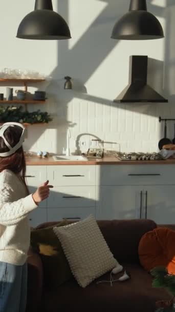 Dans un appartement ensoleillé, une fille vibrante utilise un casque de réalité virtuelle. Images 4k de haute qualité - Séquence, vidéo
