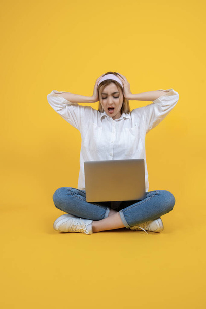Shocked young woman, full body length portrait of young shocked woman. Using reading laptop, sit floor legs crossed. Unbelievable news, clueless face expression, hold head with hands, open mouth. - Photo, Image