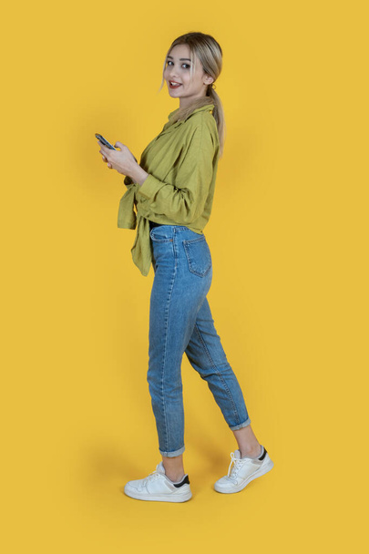 Using mobile phone device, full length body size side view young woman using mobile phone device. Attractive cheerful happy girl browsing web, social media, messaging, typing while walking. Copy space - Photo, Image