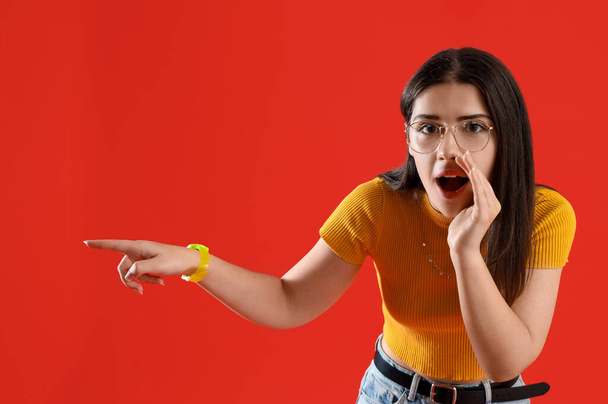 Young gossip woman pointing at something on red background - Photo, Image
