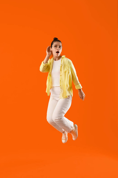 オレンジ色の背景で何かを聞こうとしている若いゴシップの女性をジャンプ - 写真・画像