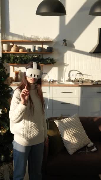 Egy napsütötte lakásban egy dinamikus lány virtuális valóság headsetet visel. Kiváló minőségű 4k felvételek - Felvétel, videó