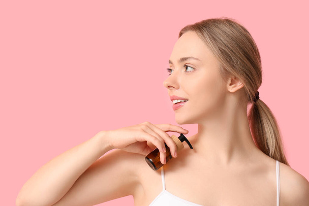 Krásná mladá žena s lahví kosmetického přípravku na růžovém pozadí - Fotografie, Obrázek
