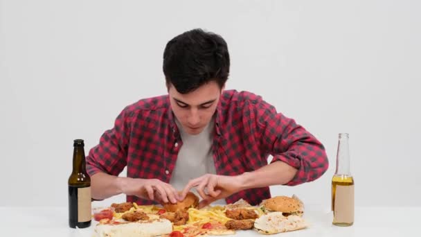 コーカサス人の男性はテーブルに座り,それぞれの噛み付きのおいしいバーガーの味を味わいます. 彼の焦点を当てた表現は,食事にふける喜びを反映しています. - 映像、動画