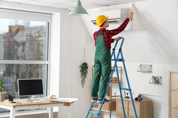 Mannelijke elektricien werkt aan trapladder in kamer, achteraanzicht - Foto, afbeelding