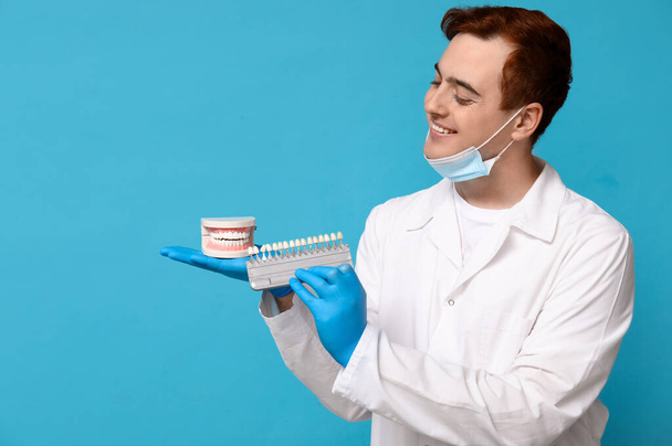 Dentiste masculin avec modèle de mâchoire et guide de teinte dentaire sur fond bleu. Journée mondiale des dentistes - Photo, image