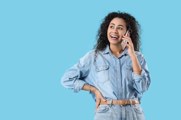 Νεαρή Αφρο-Αμερικανίδα μιλάει από κινητό τηλέφωνο σε μπλε φόντο - Φωτογραφία, εικόνα
