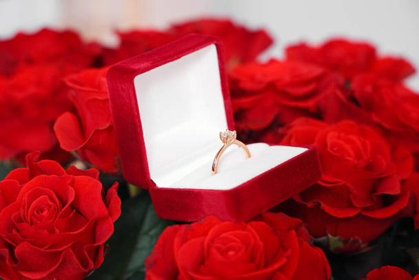 Box with engagement ring on bouquet of roses, closeup. Valentine's Day celebrations - Photo, Image