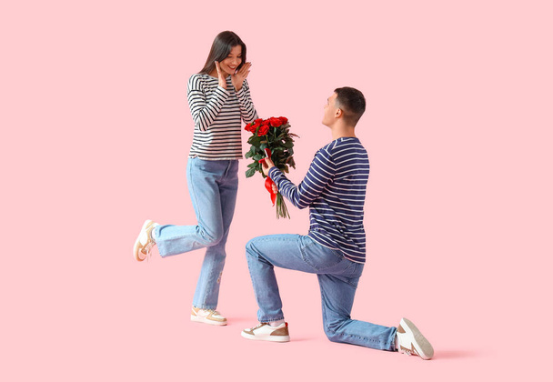 Junger Mann macht seiner Freundin auf rosa Hintergrund einen Heiratsantrag. Valentinstag-Feier - Foto, Bild