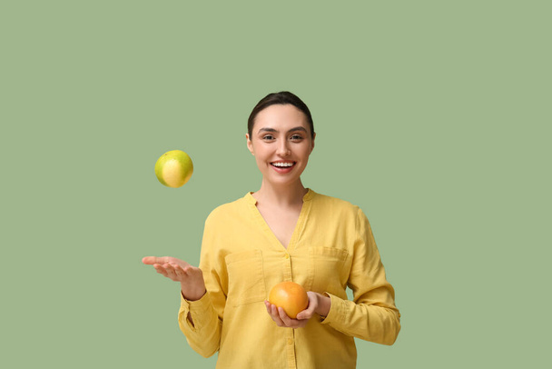 Mooie jonge vrouw met verse bergamot en grapefruit op groene achtergrond - Foto, afbeelding