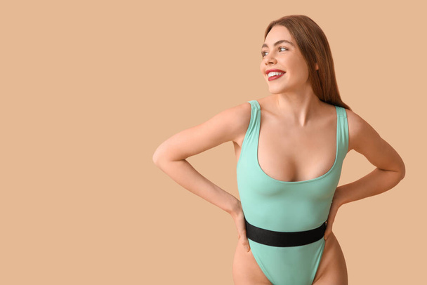 Beautiful young woman in tank swimsuit on beige background - Photo, Image