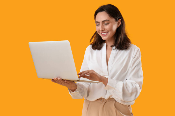 Hezká mladá žena pracující s notebookem na oranžovém pozadí - Fotografie, Obrázek