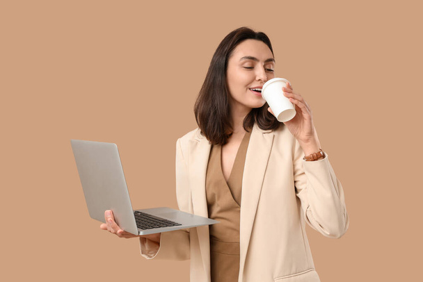 Молодая деловая женщина с ноутбуком и чашкой кофе на бежевом фоне - Фото, изображение