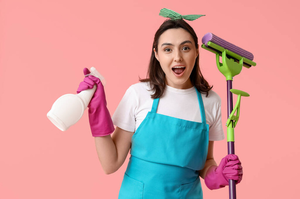 Pretty young woman with mop and bottle of detergent on pink background - Photo, Image