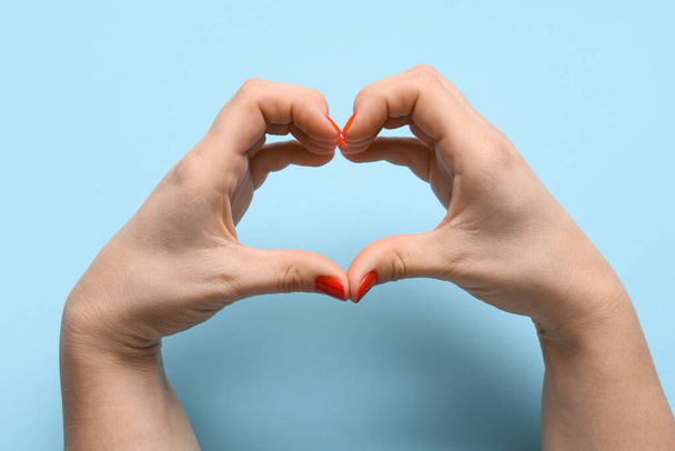 Female hands with red manicure making heart shape on blue background. Valentine's Day celebration - Photo, Image