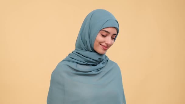 En un retrato tierno, una mujer árabe reservada exuda timidez sobre un fondo beige suave, capturando un momento de modestia silenciosa y creando una atmósfera de encanto discreto.. - Metraje, vídeo