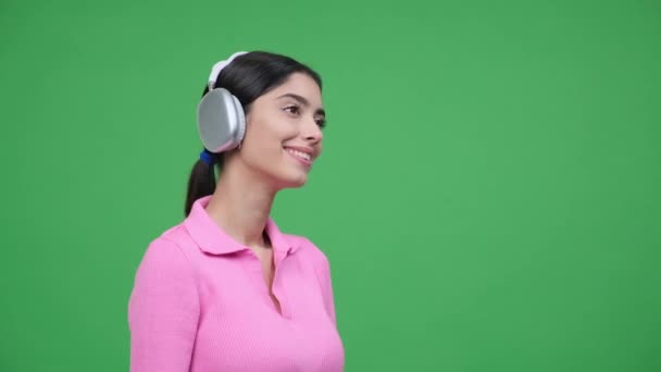 A zöld háttérben profilban rögzített nő fejhallgatót visel, elmerülve a zene örömében. Sugárzó mosolya tükrözi a dallam örömét, harmonikus és vidám jelenetet teremtve.. - Felvétel, videó