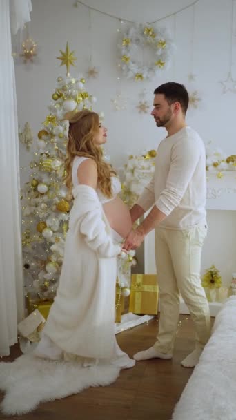De man omhelst zijn mooie glimlachende zwangere vrouw. Een stel poseert bij een fotoshoot. Kerstversiering - Video