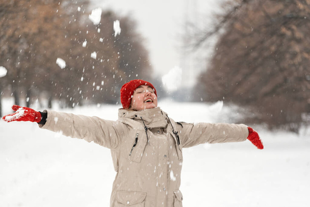 Mooi meisje heeft plezier in besneeuwd park. Vrouw in modieuze winterkleding houdt van wandelen in de winter buiten. - Foto, afbeelding