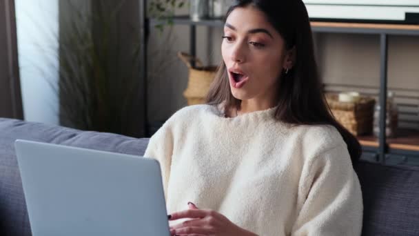 Mujer blanca radiante abraza la felicidad mientras se utiliza el ordenador portátil en la sala de estar. La vibrante atmósfera captura la esencia de la positividad, convirtiendo el espacio en un remanso de alegre compromiso. - Imágenes, Vídeo