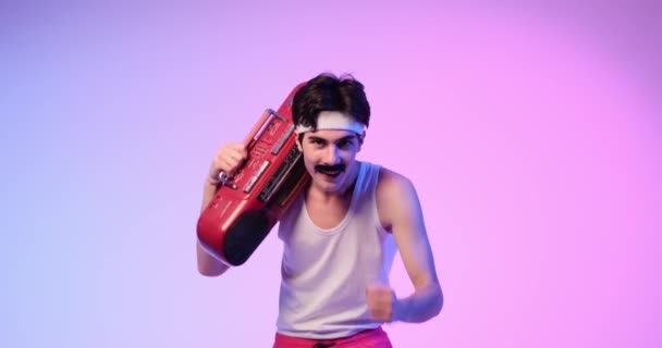 Caucasian 80s man, with a cassette player, dancing with joy and style on purple background. Showing retro dance and music, radiating positive energy and vintage coolness. - Footage, Video