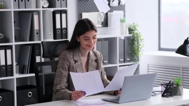 Een toegewijde blanke kantoormedewerker beheert op efficiënte wijze papieren aan haar bureau. Dit beeld weerspiegelt de positieve en productieve energie die ze bijdraagt aan de werkplek. - Video