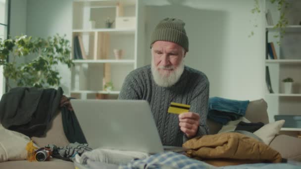 Счастливый старик путешествует делает покупки в интернет-магазине с кредитной карточкой. Пожилой человек потребитель в шляпе платить за покупку в веб-магазине. Онлайн транзакции. - Кадры, видео