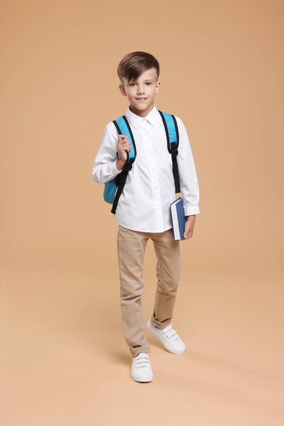 Cute schoolboy with book walking on beige background - Zdjęcie, obraz