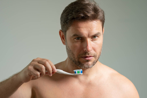 Mies soveltamalla hammastahnaa harjalla kylpyhuoneessa, lähikuva. Viehättävä mies katselee hammastahnaa ja harjaa. Huolehdin hampaista ja suusta. Hammashygienia, elinvoimaisuus ja kauneus käsitteet - Valokuva, kuva
