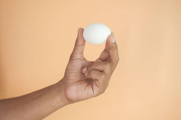 close up of men hand holding a egg against orange color background . - Photo, Image