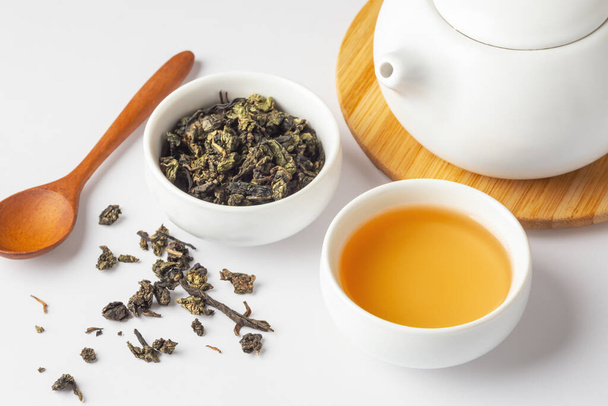 Чашка чаю і сушений чай залишають з чайником і ложкою на білому столі, крупним планом - Фото, зображення