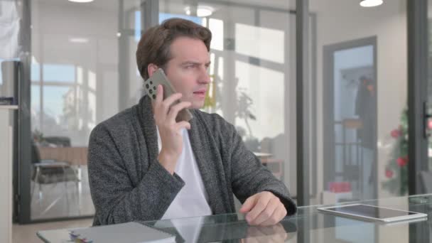 若い男はオフィスで電話で話している - 映像、動画