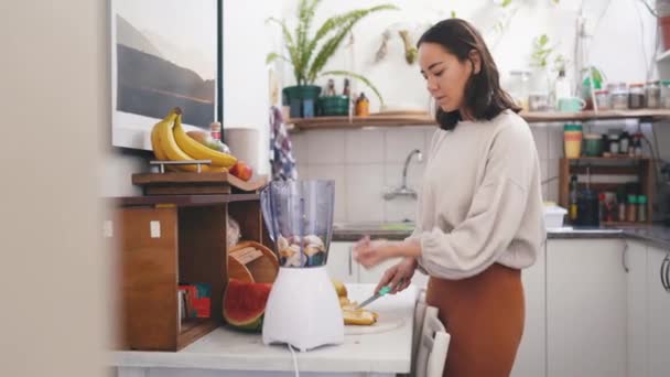 Smoothie, kuchyň a žena krájejí ovoce pro zdraví, wellness a dietní koktejl doma. Lednice, mixér a mladá asijská žena připravuje výživu, organické nebo čerstvé šťávy pro občerstvení v bytě. - Záběry, video